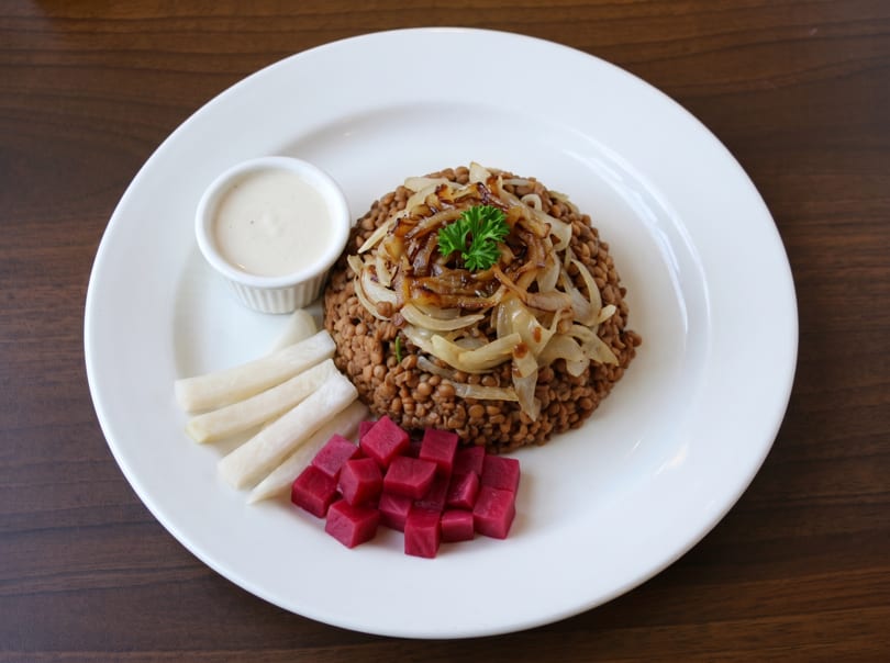 Mujadara with caramelized onions, parsley, a side of tahini sauce, white pickles, and pink pickled turnips.