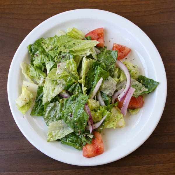 Fresh green salad with lettuce, red onion, and tomatoes, lightly dressed and seasoned with pepper.