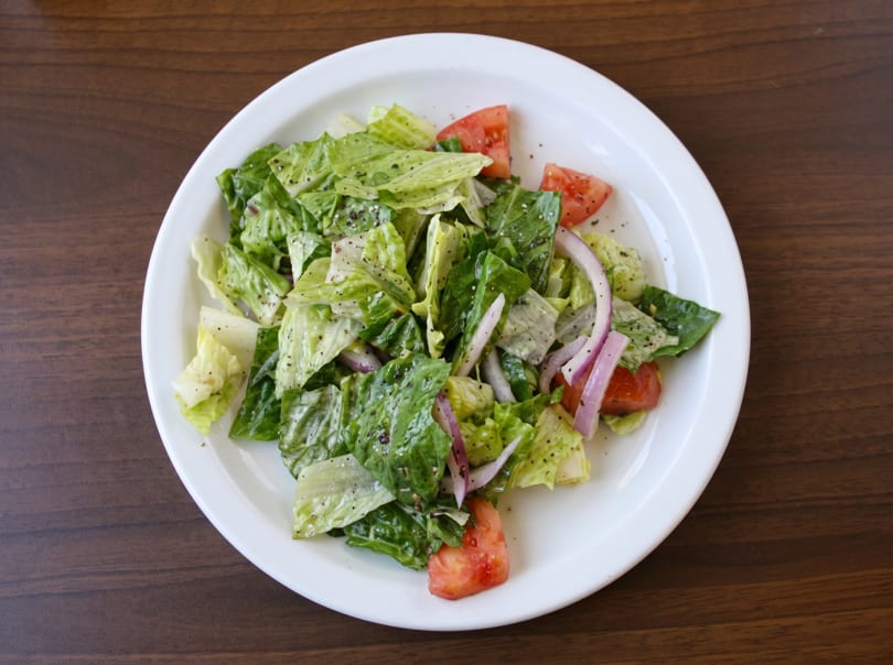 Fresh green salad with lettuce, red onion, and tomatoes, lightly dressed and seasoned with pepper.