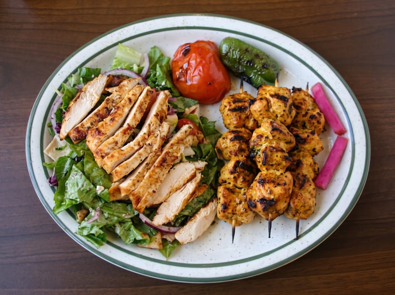 Grilled chicken breast and chicken skewers with salad, roasted tomato, pepper, and pickled turnips.