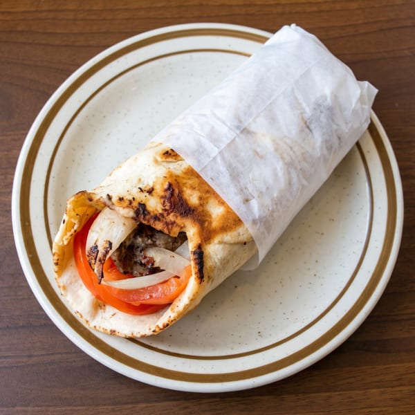 A partially unwrapped gyro with meat, tomatoes, and onions on a speckled plate.
