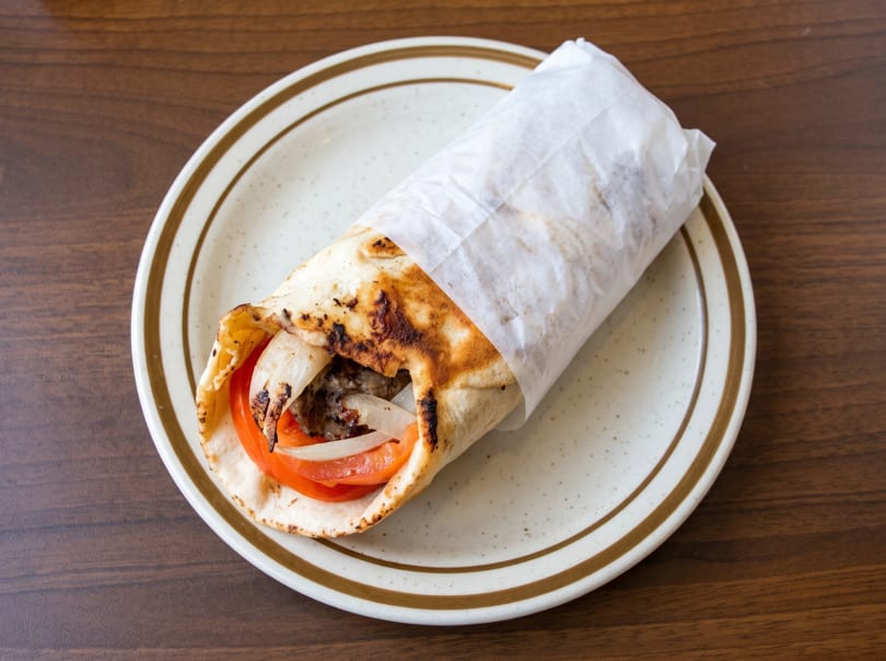 A partially unwrapped gyro with meat, tomatoes, and onions on a speckled plate.